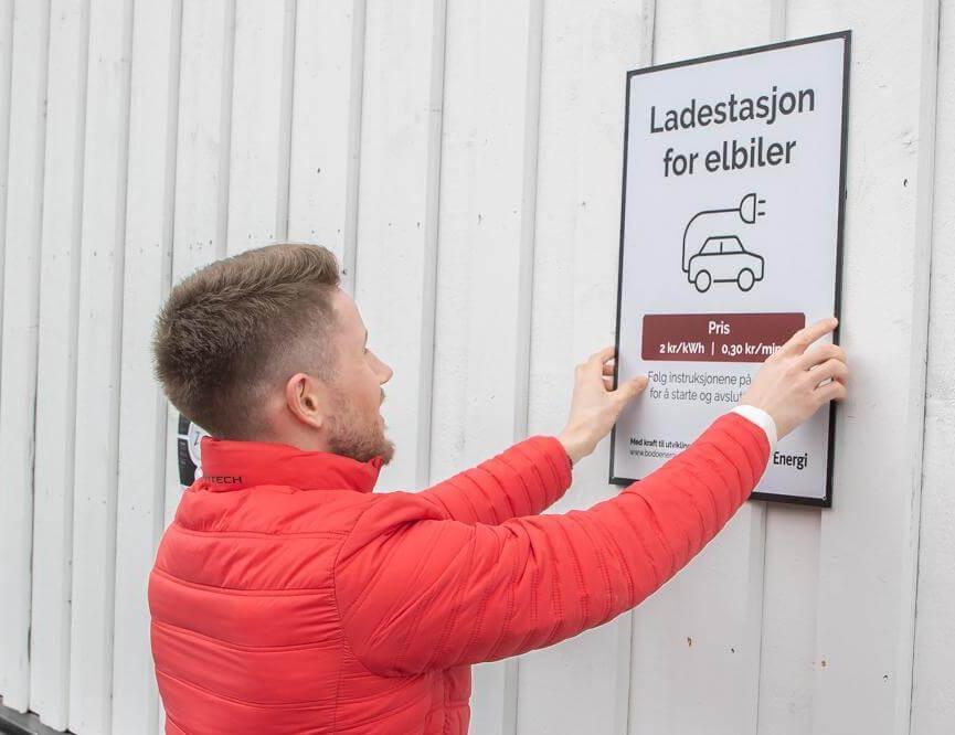 Erling Aalvik henger opp skiltet som forteller gjestene at nå kan du lade bilen din på Kjerringøy Bryggehotell